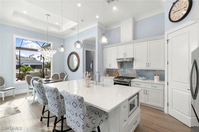 kitchen with stainless steel appliances, a sink, white cabinets, light countertops, and decorative light fixtures