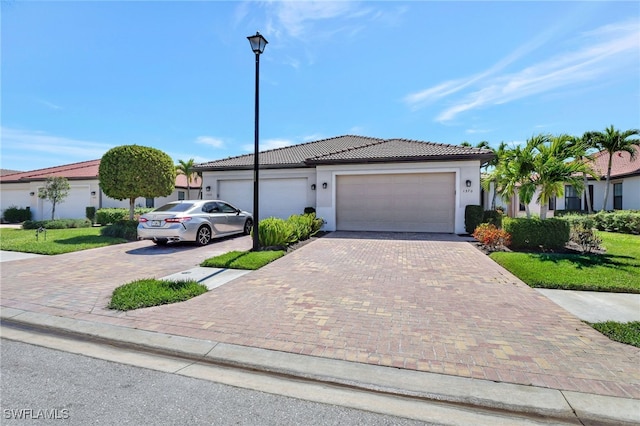 ranch-style house featuring a tiled roof, stucco siding, an attached garage, and decorative driveway