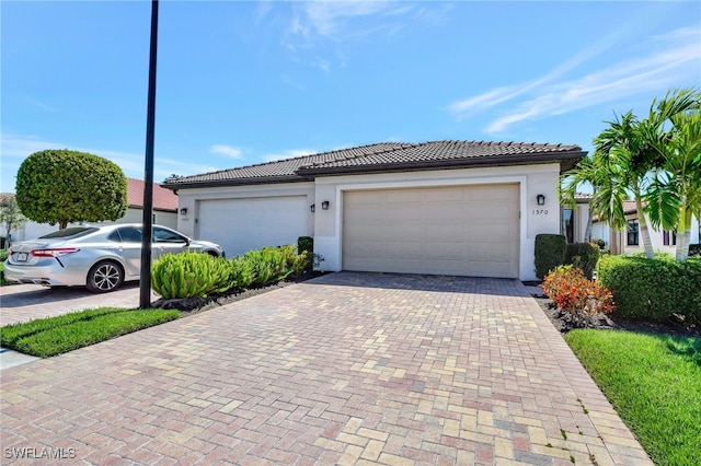 view of front of property featuring a tile roof, decorative driveway, an attached garage, and stucco siding