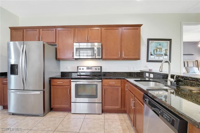 kitchen featuring dark stone counters, brown cabinets, appliances with stainless steel finishes, and a sink