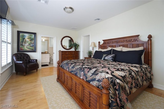 bedroom featuring light wood-style flooring, ensuite bath, and visible vents