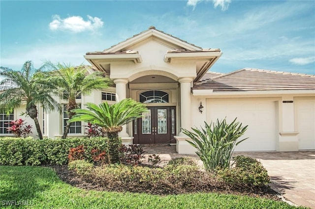 doorway to property featuring decorative driveway, french doors, an attached garage, and stucco siding