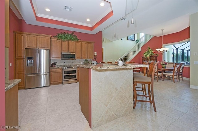 kitchen with a breakfast bar, hanging light fixtures, appliances with stainless steel finishes, a tray ceiling, and brown cabinetry