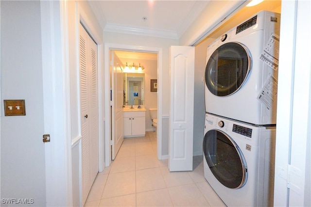 laundry area with crown molding, light tile patterned flooring, a sink, stacked washing maching and dryer, and laundry area