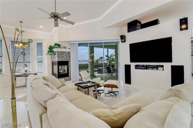 living area featuring a tiled fireplace, ornamental molding, light tile patterned flooring, baseboards, and ceiling fan with notable chandelier