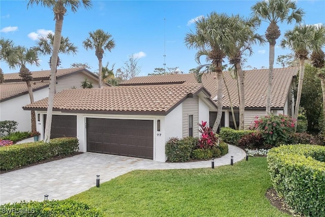 mediterranean / spanish-style house featuring a garage, a tile roof, decorative driveway, a front yard, and stucco siding