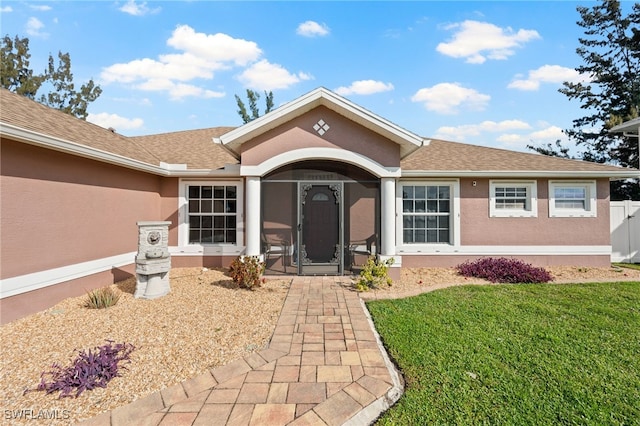 doorway to property with a yard, a shingled roof, and stucco siding