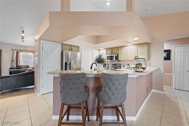 kitchen with appliances with stainless steel finishes, light countertops, a breakfast bar area, and light tile patterned floors