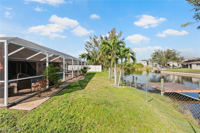 view of yard featuring a lanai, a water view, a dock, and fence