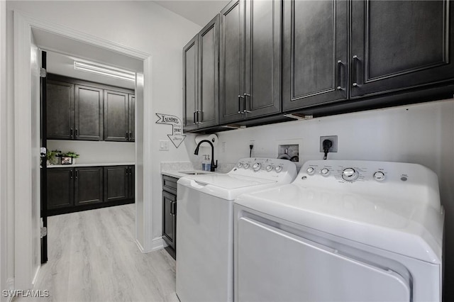 laundry room with cabinet space, light wood-style flooring, washer and dryer, and a sink