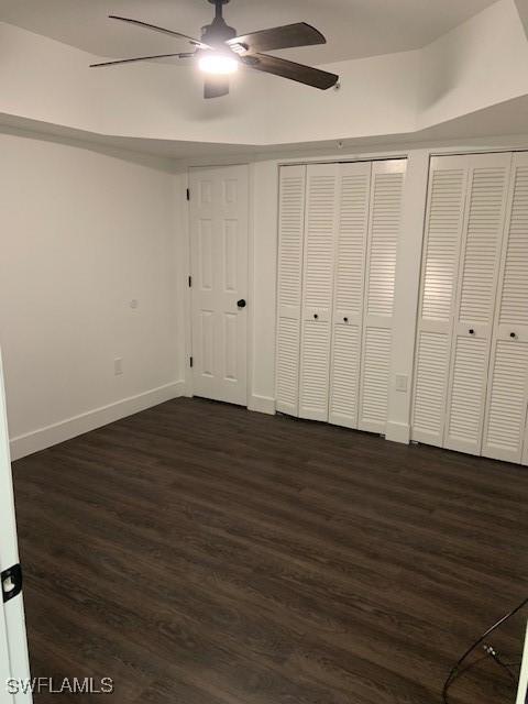 unfurnished bedroom with dark wood-style flooring, baseboards, a ceiling fan, and multiple closets