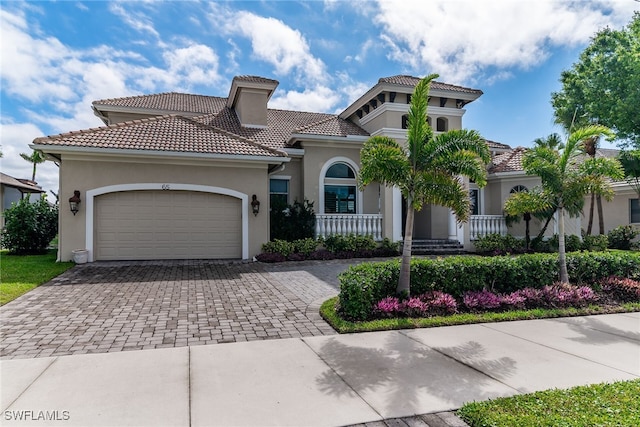 mediterranean / spanish home featuring decorative driveway, a tiled roof, an attached garage, and stucco siding