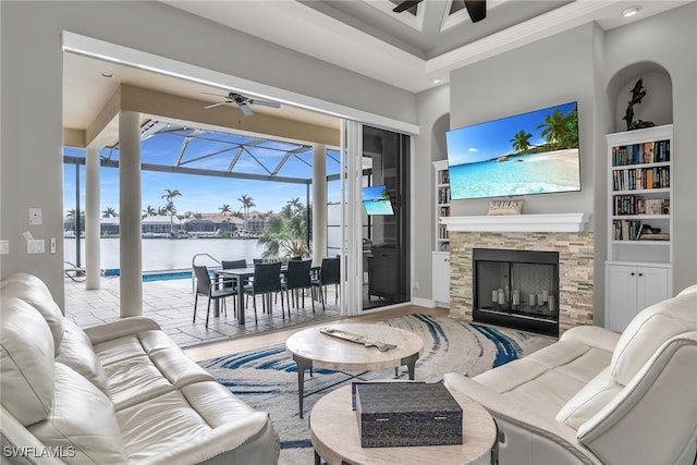 living room featuring a sunroom, ceiling fan, a fireplace, and built in shelves