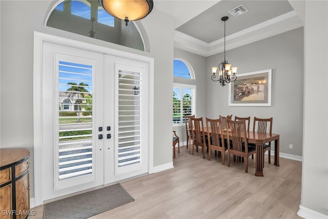 entryway with visible vents, a raised ceiling, an inviting chandelier, french doors, and light wood-style floors