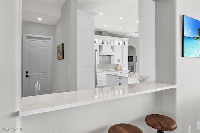 kitchen with custom exhaust hood, light countertops, white cabinets, a peninsula, and a kitchen breakfast bar