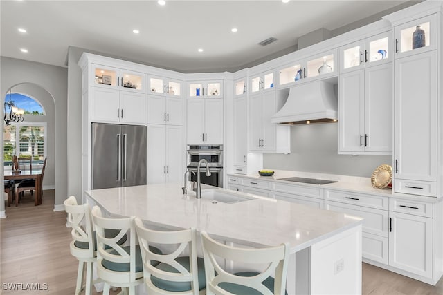 kitchen featuring a kitchen island with sink, premium range hood, appliances with stainless steel finishes, and white cabinetry