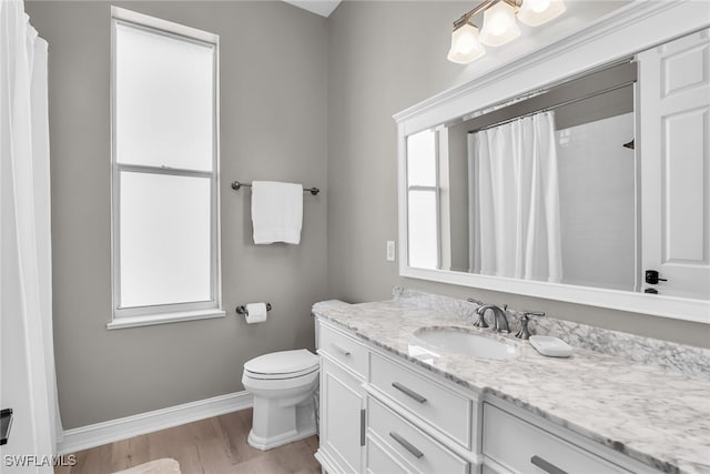 full bath with plenty of natural light, wood finished floors, vanity, and baseboards