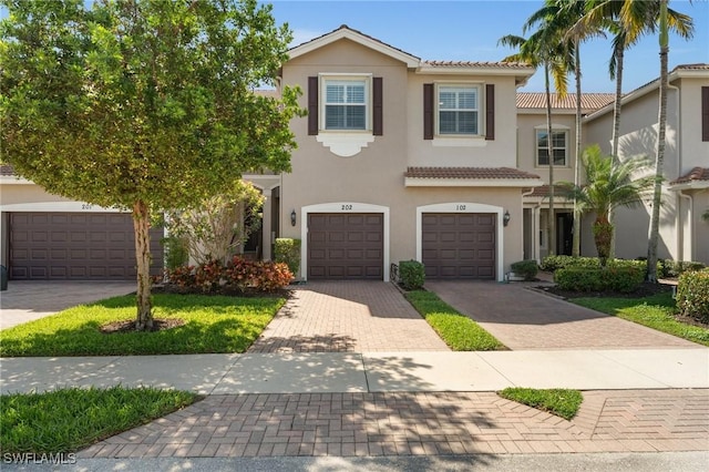 view of front of house featuring an attached garage, a tiled roof, decorative driveway, and stucco siding