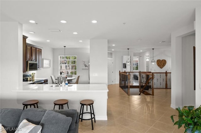 kitchen with appliances with stainless steel finishes, a breakfast bar, a peninsula, light countertops, and pendant lighting