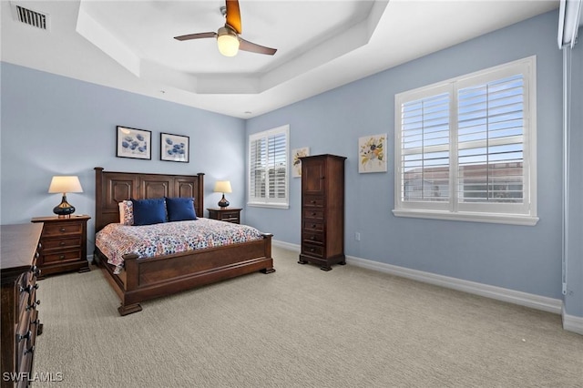 bedroom featuring light colored carpet, visible vents, a ceiling fan, baseboards, and a raised ceiling