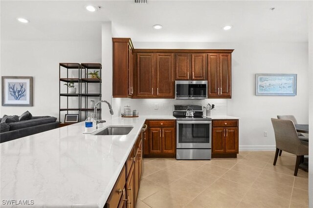 kitchen featuring a sink, open floor plan, appliances with stainless steel finishes, light stone countertops, and tasteful backsplash