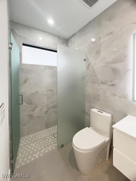 full bath with toilet, a stall shower, visible vents, and tile walls