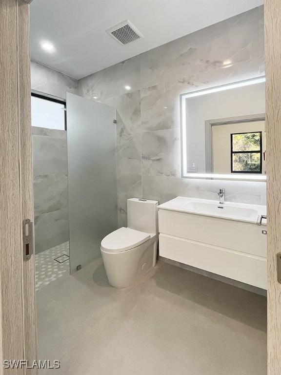 bathroom with toilet, vanity, visible vents, tile walls, and a stall shower