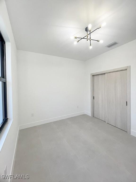 unfurnished bedroom with baseboards, visible vents, a chandelier, and a closet