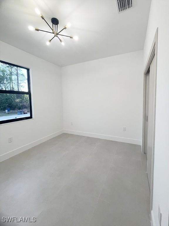 unfurnished bedroom with baseboards, visible vents, and a chandelier