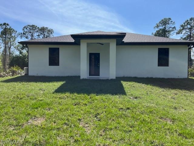 back of house with a lawn and stucco siding