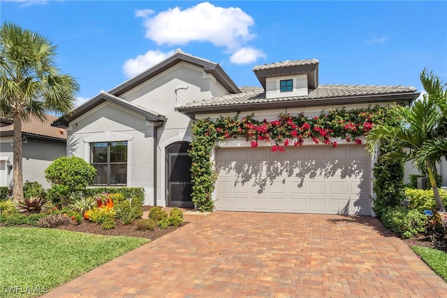 mediterranean / spanish home with a garage, stucco siding, decorative driveway, and a tiled roof