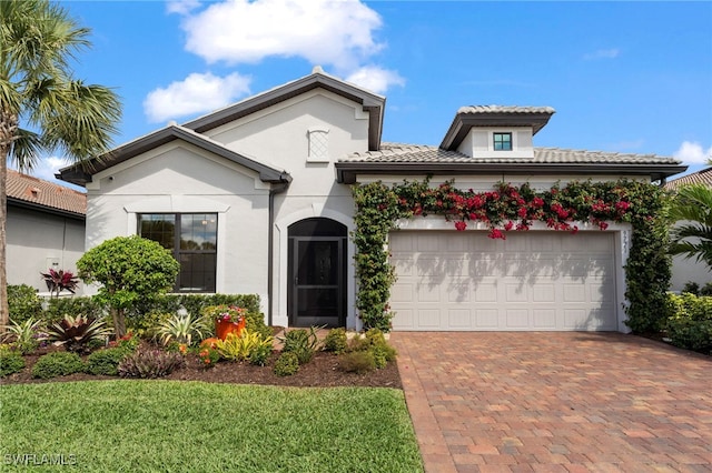 mediterranean / spanish house featuring a tiled roof, decorative driveway, an attached garage, and stucco siding