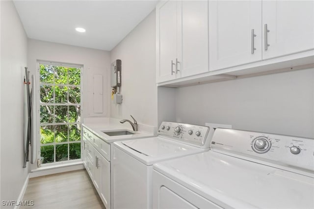 clothes washing area with cabinet space, light wood finished floors, baseboards, washing machine and clothes dryer, and a sink