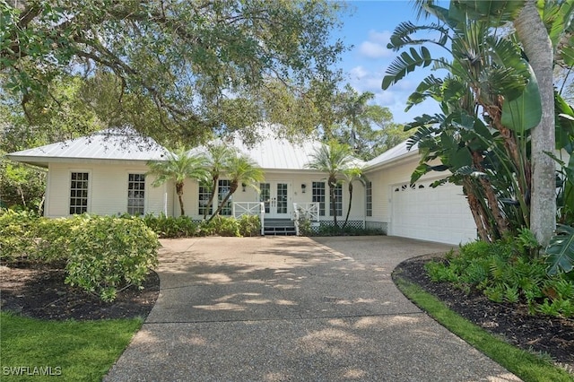 ranch-style house featuring a garage, driveway, and metal roof