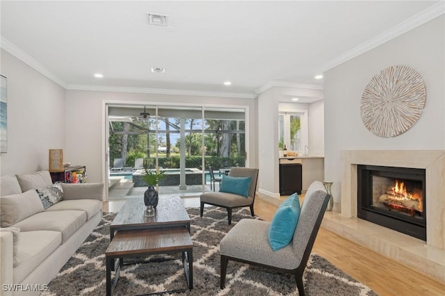 living area featuring ornamental molding, visible vents, a fireplace, and light wood finished floors