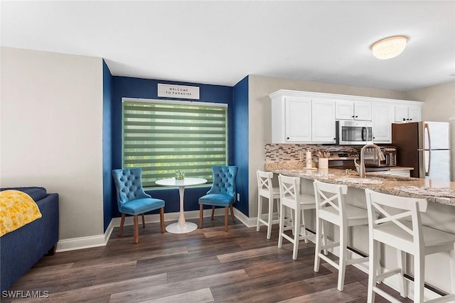 kitchen featuring tasteful backsplash, dark wood-type flooring, stainless steel appliances, a kitchen bar, and white cabinetry