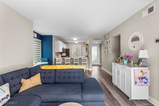 living area with a bar, dark wood-style flooring, visible vents, and baseboards