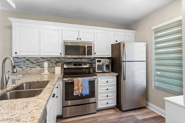 kitchen featuring light stone counters, a sink, white cabinetry, appliances with stainless steel finishes, and decorative backsplash