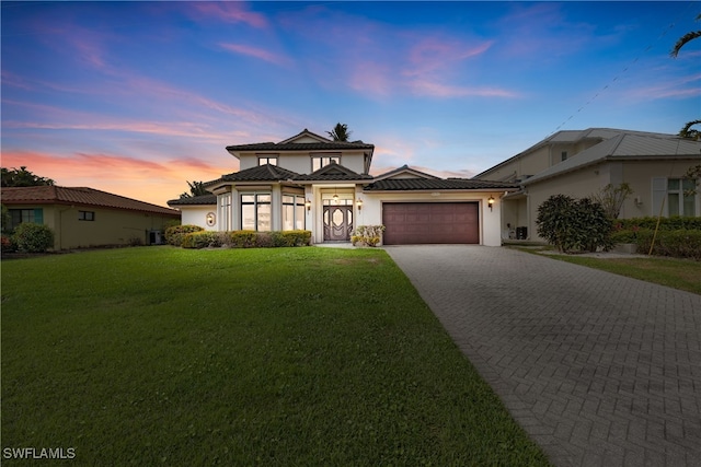 view of front of home with an attached garage, a lawn, decorative driveway, and a tiled roof