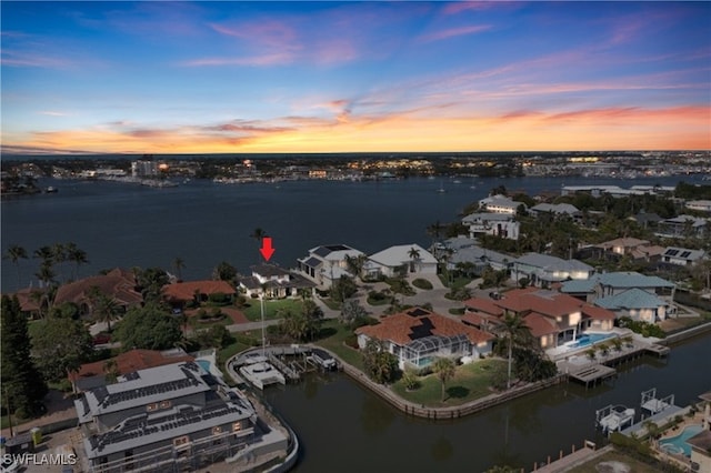 aerial view at dusk with a water view and a residential view