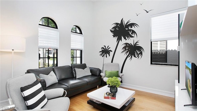 living room featuring light wood-type flooring, a towering ceiling, and baseboards