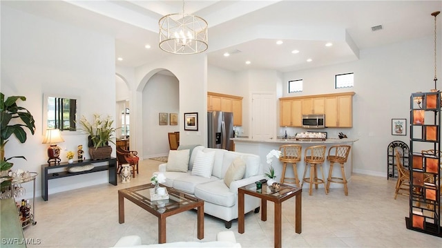 living area with visible vents, arched walkways, a towering ceiling, a notable chandelier, and a wealth of natural light