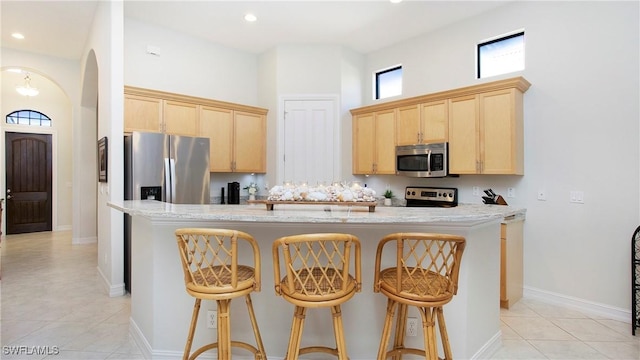 kitchen with stainless steel appliances, a high ceiling, light brown cabinetry, a kitchen island, and a kitchen breakfast bar