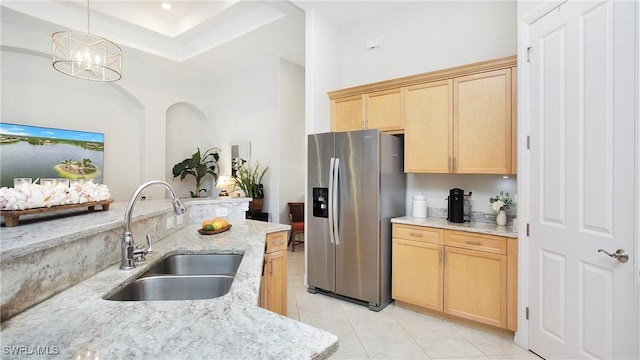 kitchen with stainless steel fridge, light stone counters, decorative light fixtures, light brown cabinets, and a sink