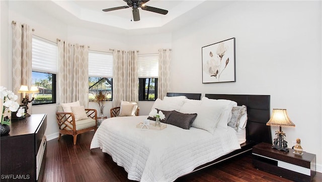 bedroom with a tray ceiling, wood-type flooring, and baseboards