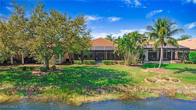 rear view of house with a lawn, a water view, and a lanai