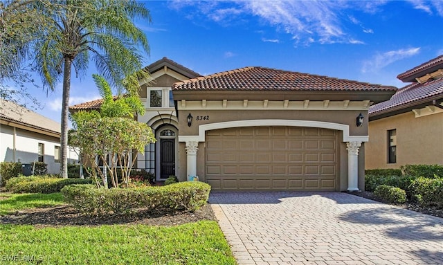 mediterranean / spanish home featuring decorative driveway, an attached garage, a tile roof, and stucco siding