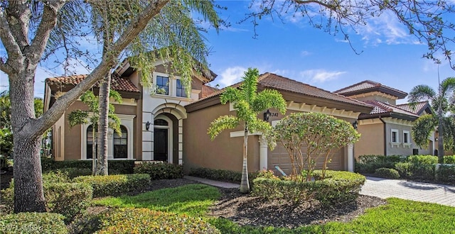 mediterranean / spanish-style home with an attached garage, a tiled roof, decorative driveway, and stucco siding