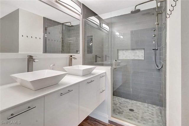 bathroom featuring wood finished floors, a sink, a shower stall, and double vanity