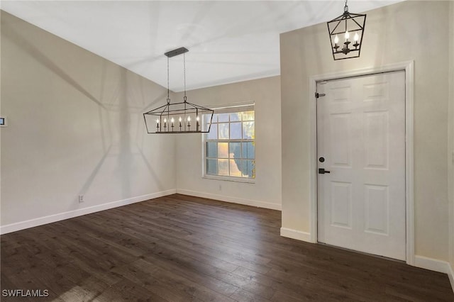 unfurnished dining area featuring dark wood-type flooring, a notable chandelier, and baseboards